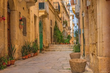 Valletta, Malta 'da sarı binaları ve saksıları olan eski dar bir ortaçağ sokağı.