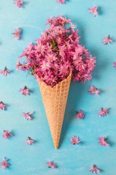 Es krim kerucut dengan cherry merah muda mekar atau bunga sakura di latar belakang biru. Berbaringlah. pemandangan atas. orientasi vertikal — Stok Foto