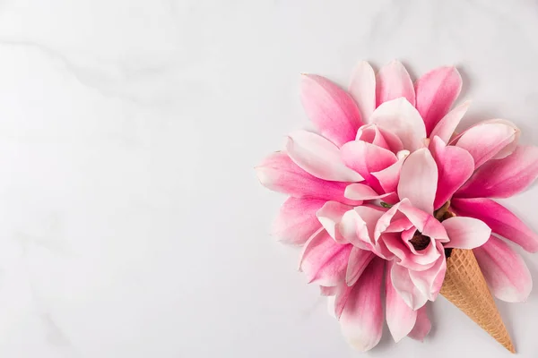 Tata letak kreatif yang dibuat dengan bunga magnolia merah muda dalam es krim kerucut pada latar belakang marmer putih. Berbaringlah. tampilan atas — Stok Foto