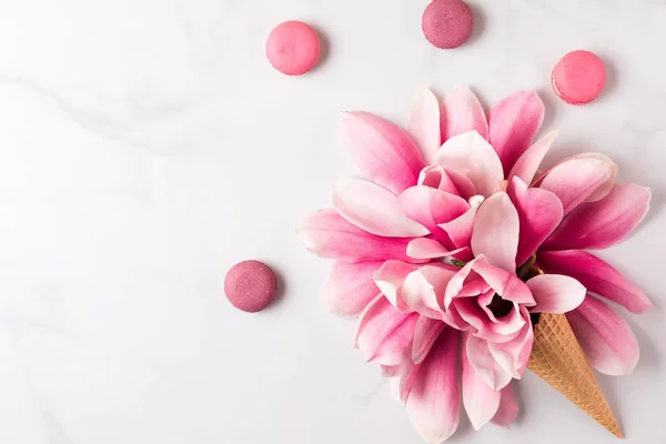 Magnolia merah muda musim semi bunga dalam wafel kerucut dengan makaroni di latar belakang putih. konsep musim semi. flat lay. tampilan atas — Stok Foto