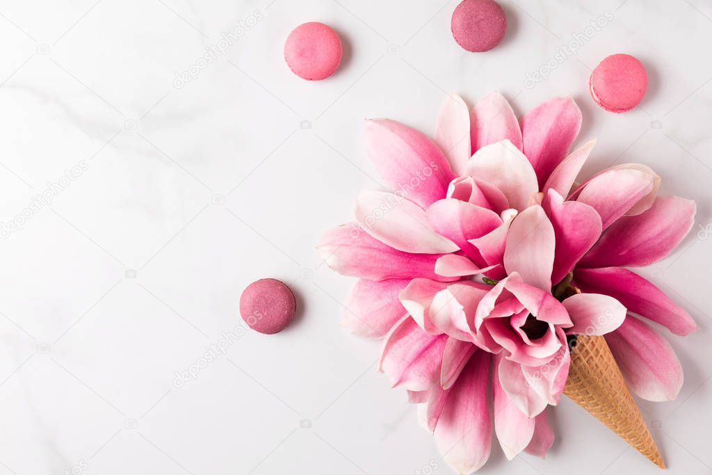 Spring pink magnolia flowers in waffle cone with macaroons on white background. spring concept. flat lay. top view