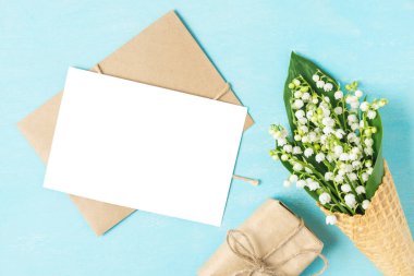 Vadi zambağı çiçekli boş tebrik kartı mavi arka planda hediye kutusuyla waffle külahında. Model yap. Düz yat. Üst Manzara. düğün davetiyesi