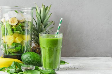Sağlıklı detoks smoothie yapmak için taze malzemelerle karıştırıcı bir kamışla hazırlanmış yeşil bir bardak içecek. Vejetaryen yemek konsepti