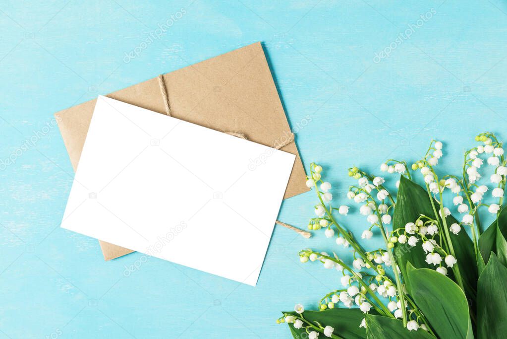 blank greeting card and envelope with spring flowers lily of the valley on blue wooden background. mock up. flat lay. top view with copy space. wedding invitation