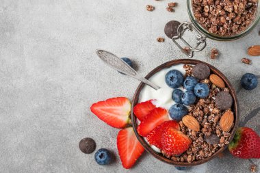 Bir kase yulaf ezmeli yoğurt, taze yaban mersini, çilek ve sağlıklı kahvaltı için gri arka planda kaşıkla fındık. Kopyalama alanı olan üst görünüm