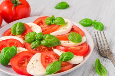 Olgun domatesli Caprese salatası ve çatallı taze fesleğen yapraklı mozzarella peyniri. İtalyan yemeği. en üstteki görünüm