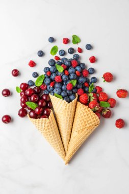 Beyaz mermer masada yabanmersini, ahududu, çilek ve vişneli dondurma külahları. Düz yat. Üst Manzara. Yaz yemekleri konsepti. düşey yönelim