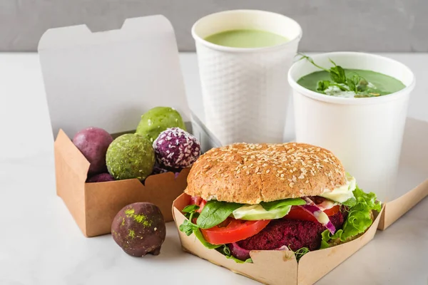 Food delivery. Vegan beet burger and energy balls in eco paper boxes with pea cream soup and matcha latte in disposable cups. Healthy diet lunch to take away