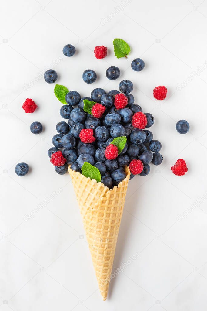 wildberries blueberry and raspberry with mint in waffle ice cream cone on white marble background. summer food concept. top view. flat lay. vertical orientation