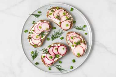 Beyaz mermer masada yumuşak peynirli, soğanlı ve dereotlu turp tostları. Sağlıklı beslenme atıştırmalıkları. en üstteki görünüm