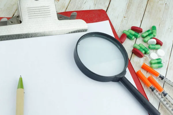 Hand write on a blank paper with medicine and magnifying glass om wooden background