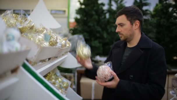 Ο άνθρωπος επιλέγει διακοσμήσεις Χριστουγέννων σε ένα κατάστημα — Αρχείο Βίντεο