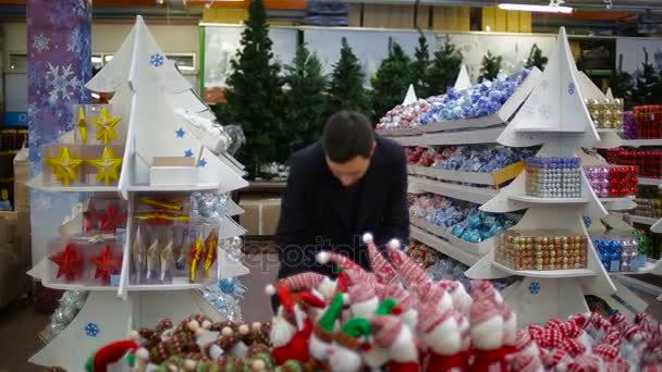 Человек выбирает рождественские игрушки в супермаркете — стоковое видео