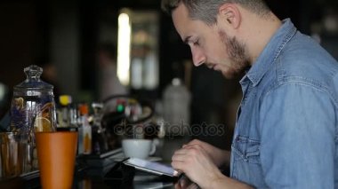 Genç bir adam barda otururken tablet kullanır