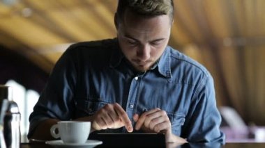 Genç bir adam barda otururken tablet kullanır
