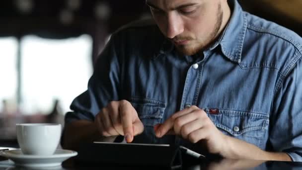 Joven escribiendo en una tableta mientras está sentado en el bar — Vídeo de stock