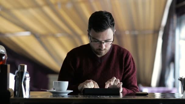Homem jovem digitando em um tablet enquanto sentado no bar — Vídeo de Stock