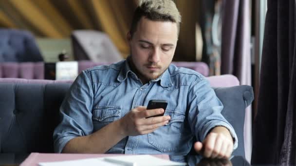 Hombre sentado en el restaurante, mensajes de texto en el teléfono móvil y sonriendo — Vídeos de Stock