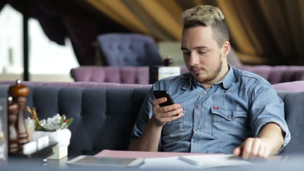 Homem sentado no restaurante, mensagens de texto no telefone celular e sorrindo — Vídeo de Stock