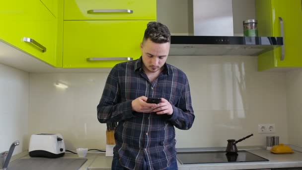 Jovem usando smartphone por mesa na cozinha — Vídeo de Stock