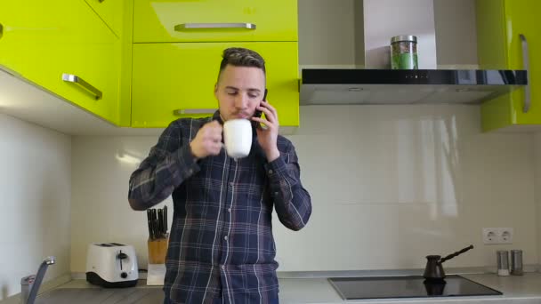 Jonge man praten op mobiel en drinken koffie in keuken thuis — Stockvideo