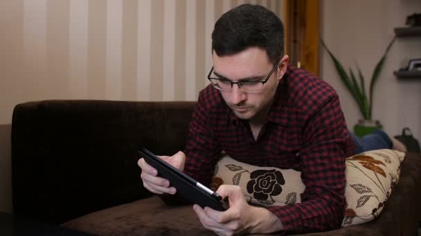 성인 남자 보고 연주 게임 디지털 태블릿을 사용 하 여 소파에 편안한 — 비디오