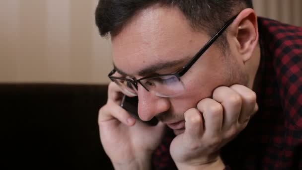 Мужчина грустит, разговаривая по телефону, лежа на диване — стоковое видео