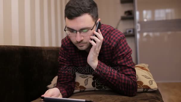 Vonzó fiatal férfi gyártás egy telefon hív, egy számítógép tabletta, a kezében — Stock videók