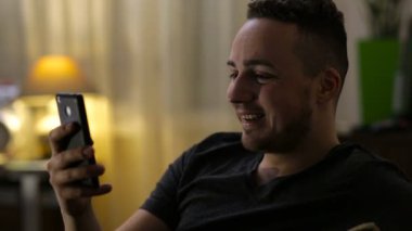 Genç, mutlu adam Smartphone'da evde gece tarafından sohbet