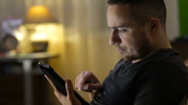 Tabletli bir adam evdeki kanepede oturuyor.