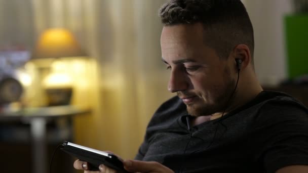 Hombre viendo vídeo o escuchando música en la tableta en casa — Vídeo de stock