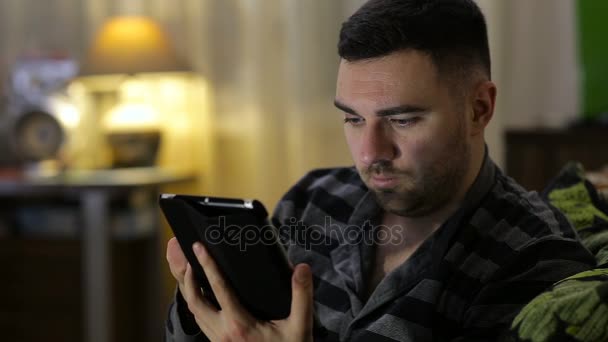 Άνθρωπος με tablet υπολογιστή κάθεται στον καναπέ στο σπίτι — Αρχείο Βίντεο