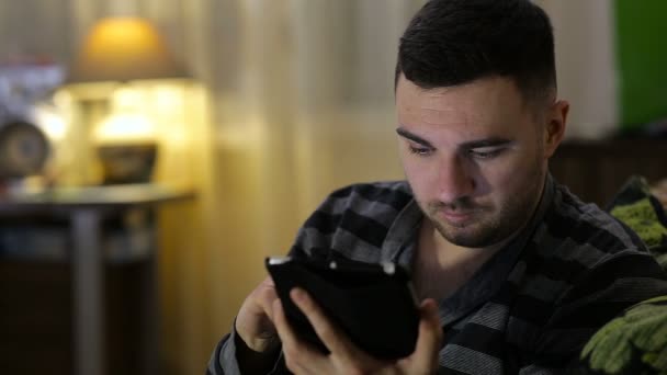 Muž s tabletovým počítačem sedící doma na pohovce — Stock video