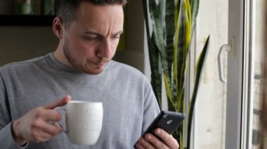 Genç bir adam sabahleyin kahve içerken cep telefonuyla konuşuyor.