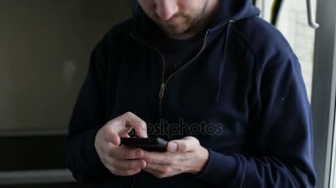 Evde cam kenarında duran ve kameraya bakarak smartphone cep telefonu ile yetişkin adam manifatura