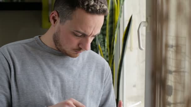 Hombre de pie con la tableta junto a la ventana en casa — Vídeos de Stock