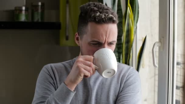 Молодой человек пьет кофе и наслаждается видом из окна — стоковое видео