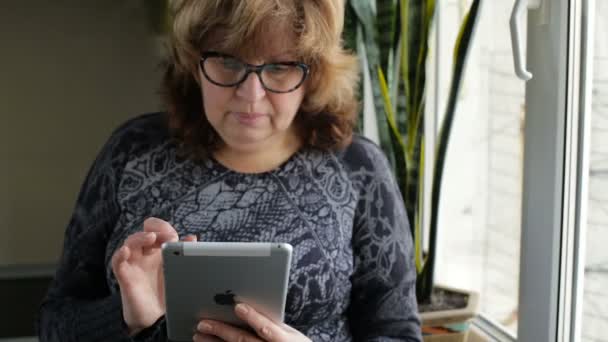 Ελκυστική ώριμη γυναίκα με υπολογιστή δισκίο περιήγηση στο internet στο σπίτι — Αρχείο Βίντεο