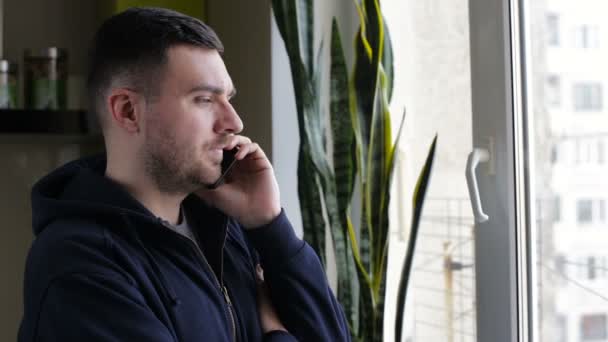 Homme parlant au téléphone debout près de la fenêtre à la maison — Video