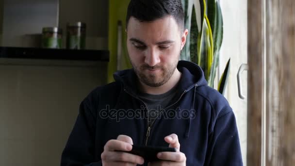 Молодий чоловік грає в гру і виграє на смартфоні вдома — стокове відео