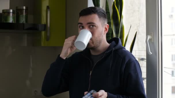 П'є ранню чашку кавового будинку, чоловік розслабляється на початку дня, затискаючи телевізор — стокове відео