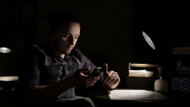 El hombre utiliza el teléfono inteligente por la noche en un café — Vídeos de Stock