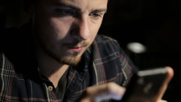 Junger Mann benutzt das Smartphone nachts in einem Restaurant in Nahaufnahme — Stockvideo