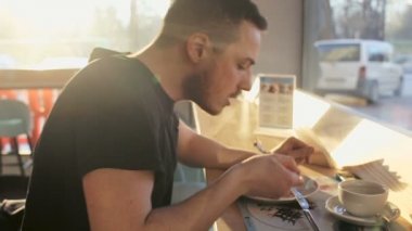 Genç adam yeme kruvasan, şehirdeki kafede kahve içme. uyuşuk