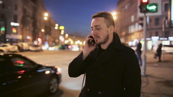 Молодой человек разговаривает по телефону на открытом воздухе ночью в городе — стоковое видео