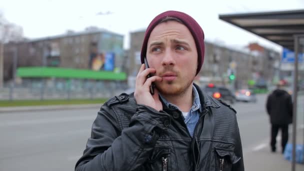 El tipo está hablando por teléfono en la parada de autobús. — Vídeo de stock
