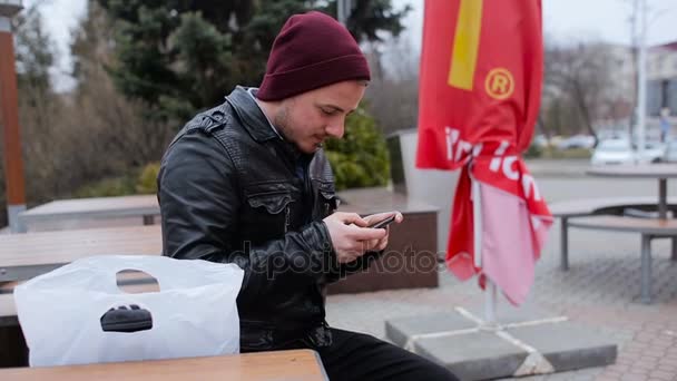 Un jeune homme assis dehors et regardant son téléphone — Video