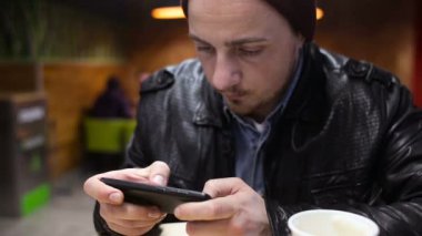 Genç, odaklı adam kafede oturan smartphone cep telefonu ile oyun oynama