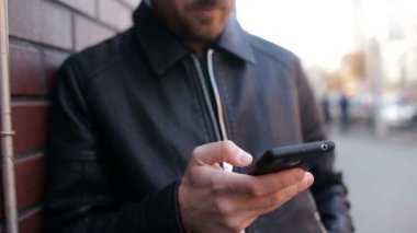 Tuğla duvar City tarafından Smartphone ayakta kullanan genç adam