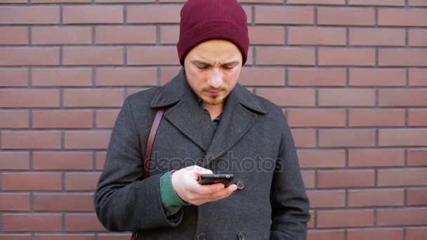 Jonge man met behulp van smartphone staande door bakstenen muur in de stad — Stockvideo